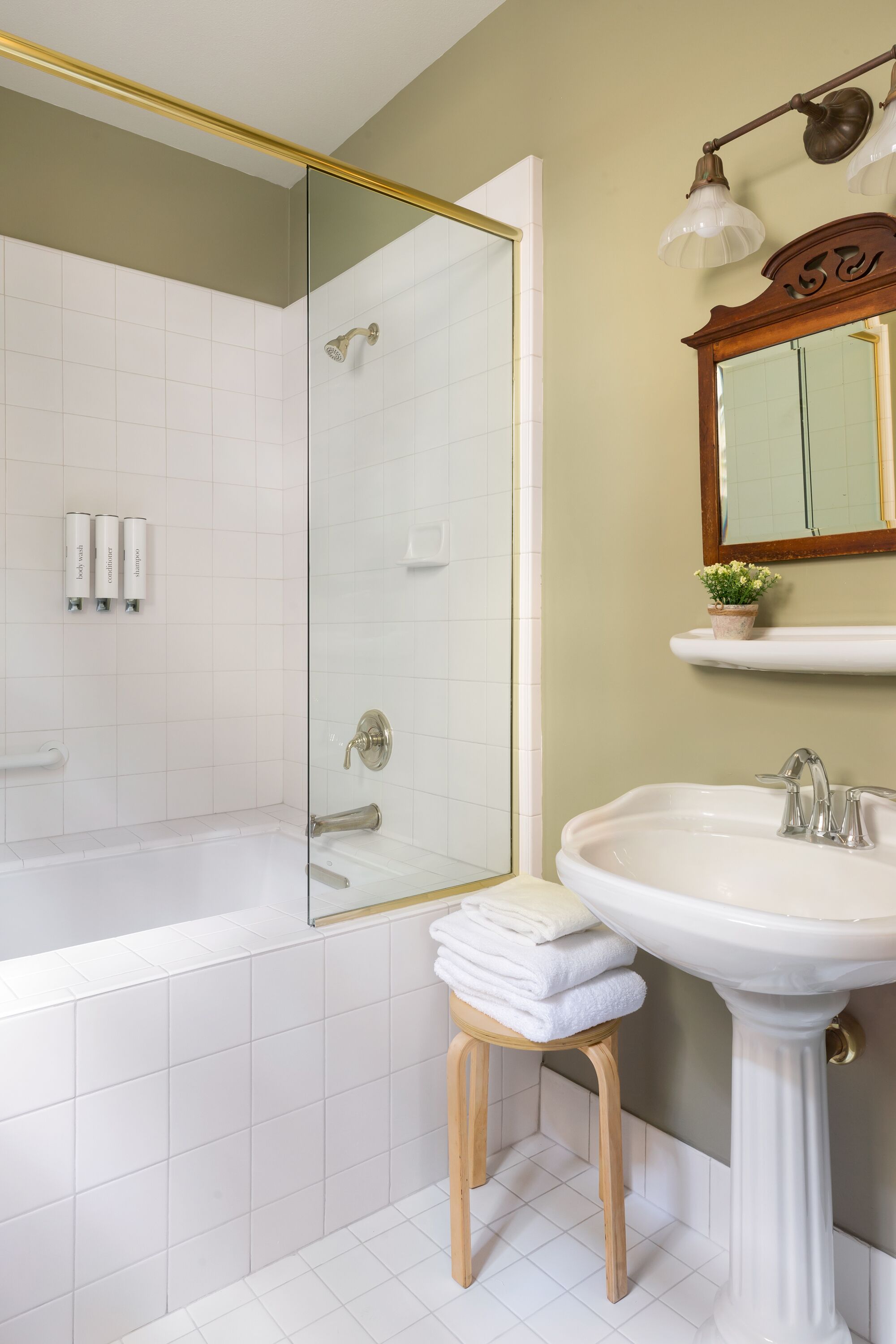 A bathroom with a glass-enclosed shower, a pedestal sink, and a mirror above the sink.