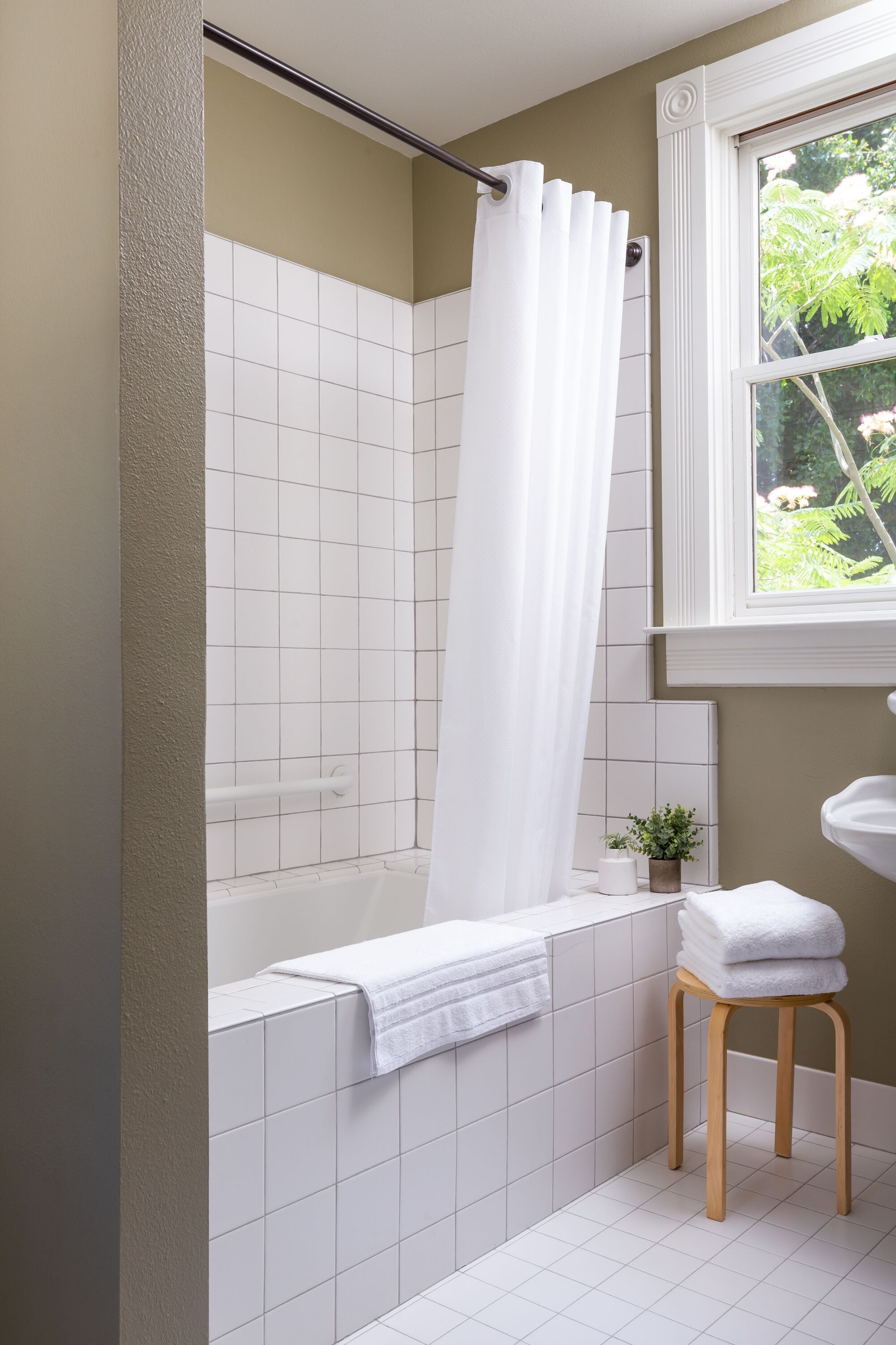 A bathroom with a bathtub, a shower curtain, a window, a sink, and a small potted plant.