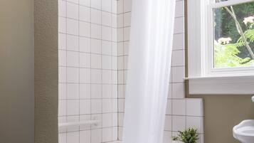 A bathroom with a bathtub, a shower curtain, a window, a sink, and a small potted plant.