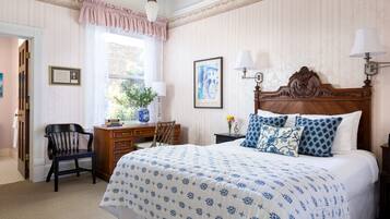 A bedroom with a large bed, a wooden desk, a chair, and a window with curtains.