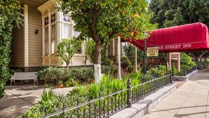 Una posada con jardín en una calle, con un toldo rojo, una banca y un jardín bien cuidado.