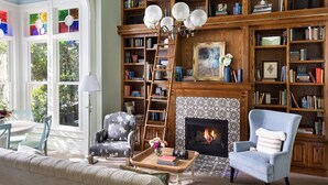 Una sala de estar acogedora con chimenea, una estantería llena de libros, un sillón cómodo y un comedor con mesa y sillas.
