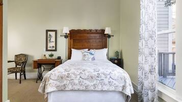 A bedroom with a wooden headboard, a floral bedspread, a desk with a lamp, and a chair.