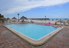 Uma piscina retangular com borda azulejada, rodeada por um terraço de tijolos.