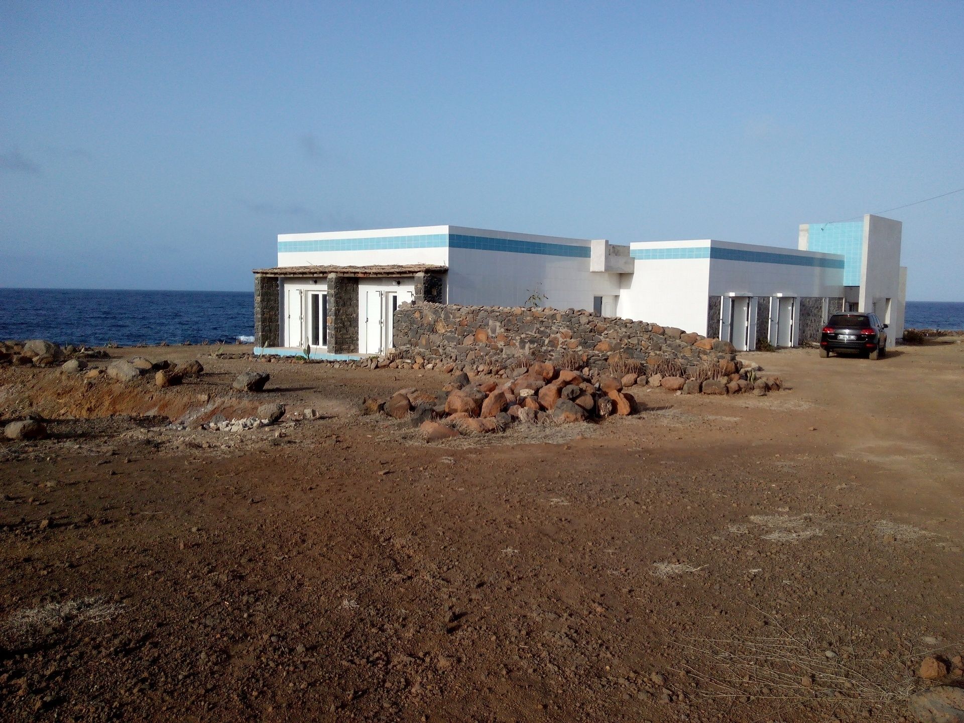 A coastal building with a stone wall and a car parked nearby.