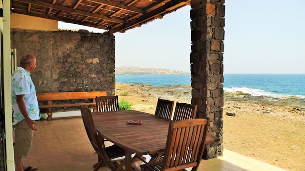 A covered outdoor dining area with stone walls and a view of the beach and sea. - Villa Sao Jose (Santa Cruz)