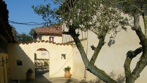 A narrow alleyway with a tree, potted plants, and a building with a tiled roof. - Le Domaine du Passage (Manciet)