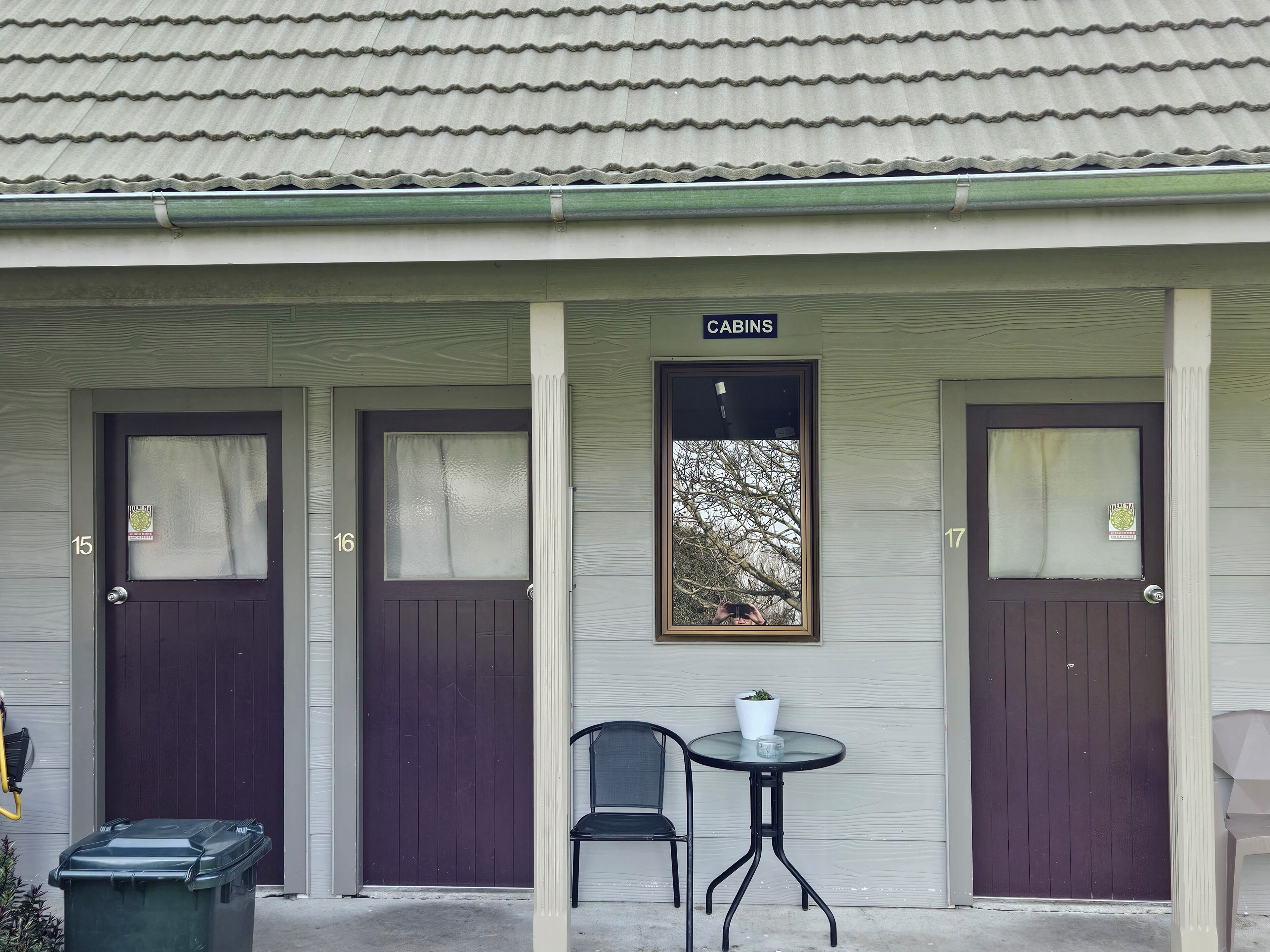 A building with three doors labeled "Cabins" and a small table with a chair in front.