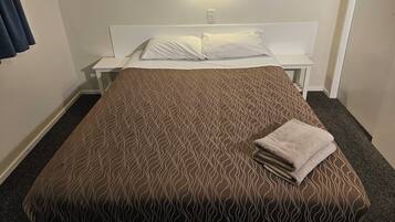 A neatly made bed with a patterned bedspread, a white pillow, and a folded towel on the side. There is a bedside table with a lamp and a wall-mounted light fixture above the bed.