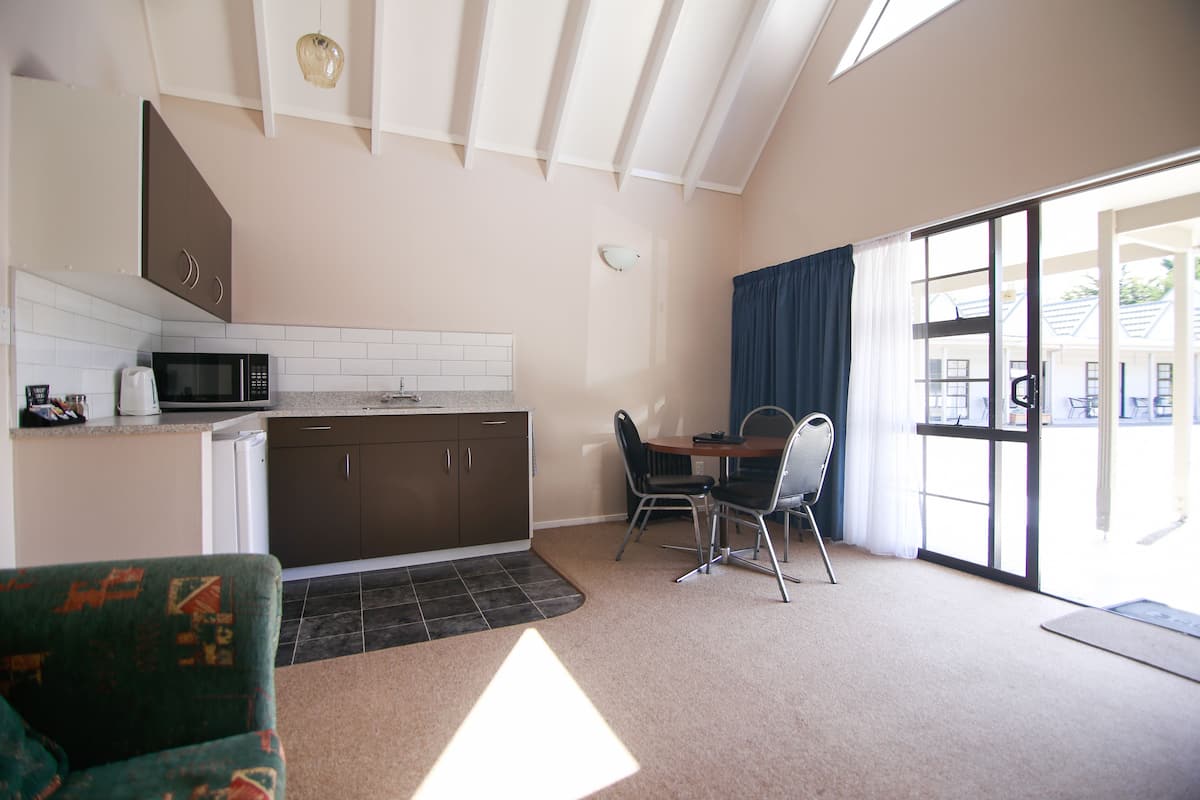 A compact kitchen with a microwave, a coffee maker, and a sink. There is a dining area with a table and chairs, and a large window with curtains.