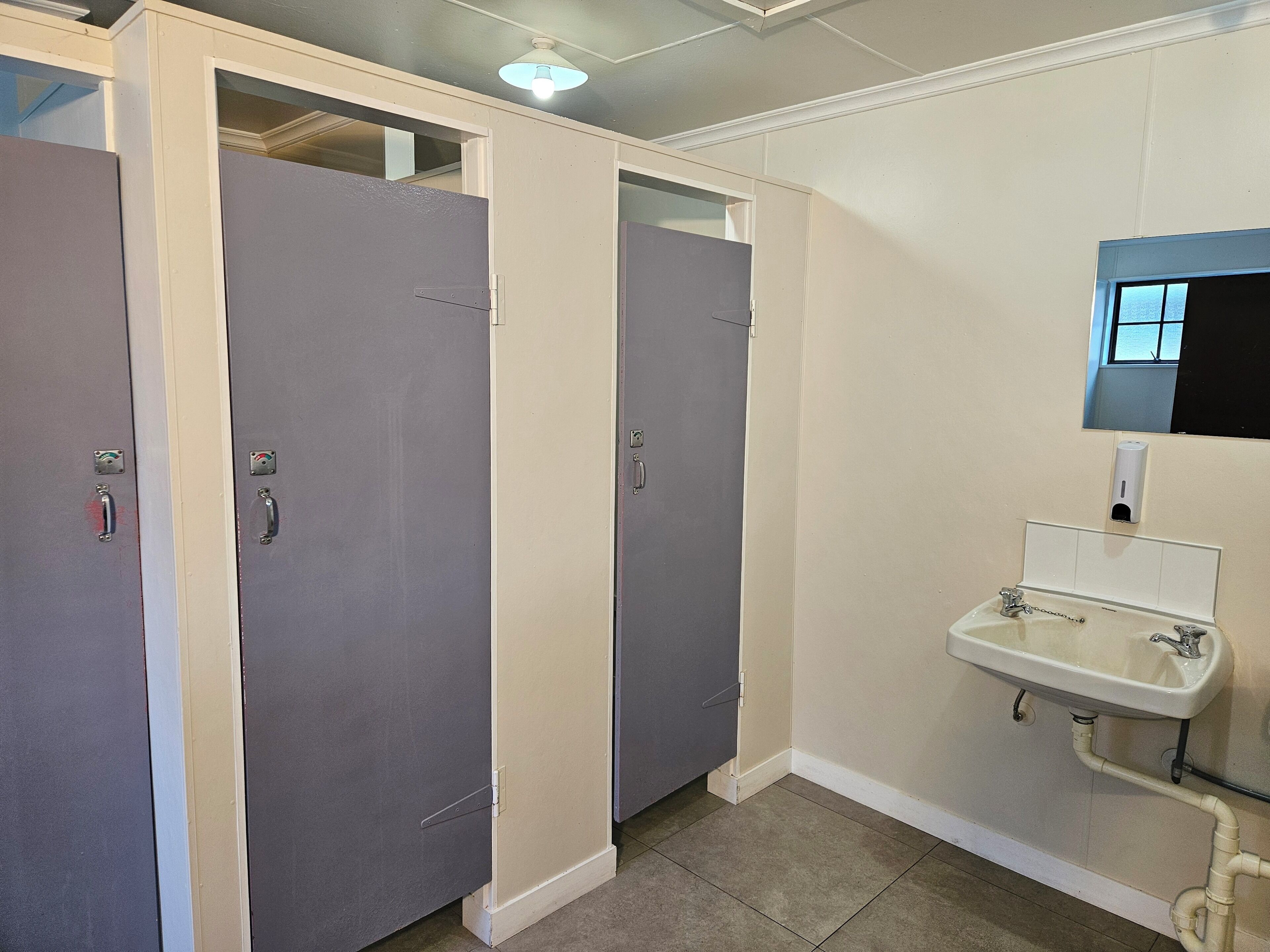 Un baño con dos puertas, un lavamanos y un espejo.