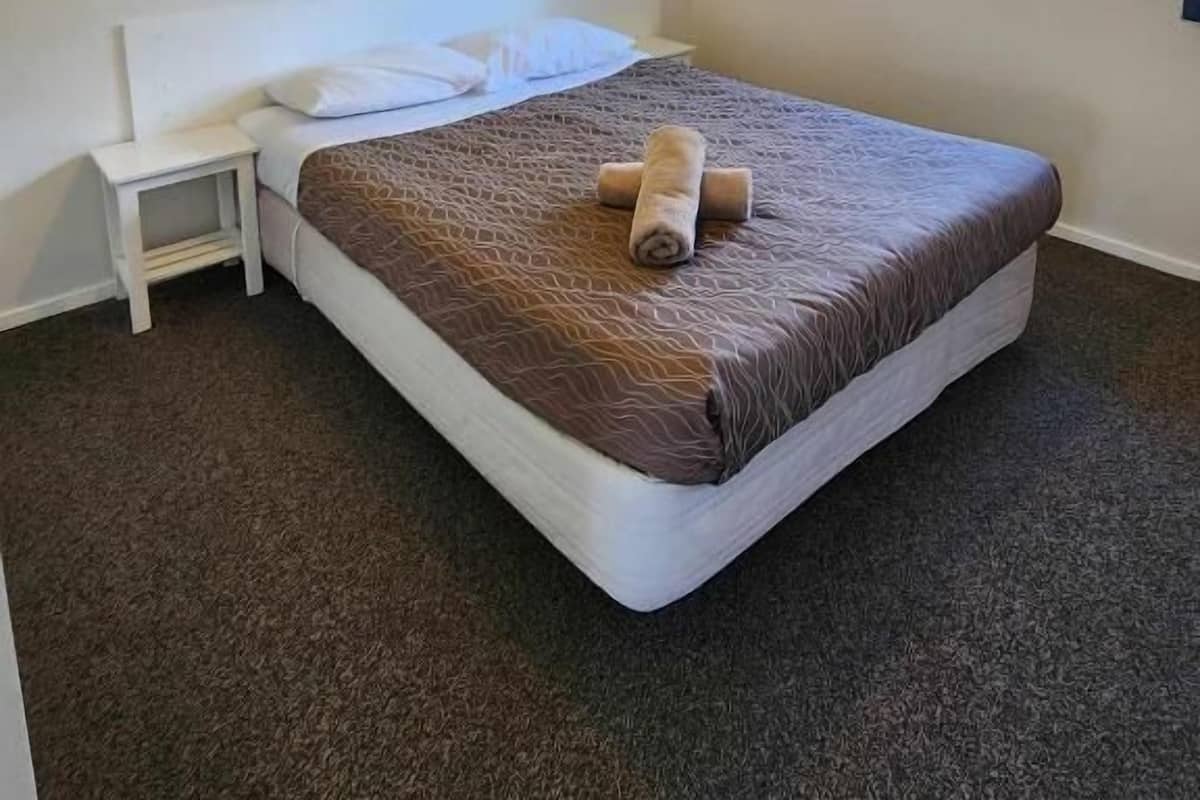 A single-bed room with a headboard, bedside table, and a window with curtains.