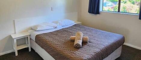 A single-bed room with a headboard, bedside table, and a window with curtains.