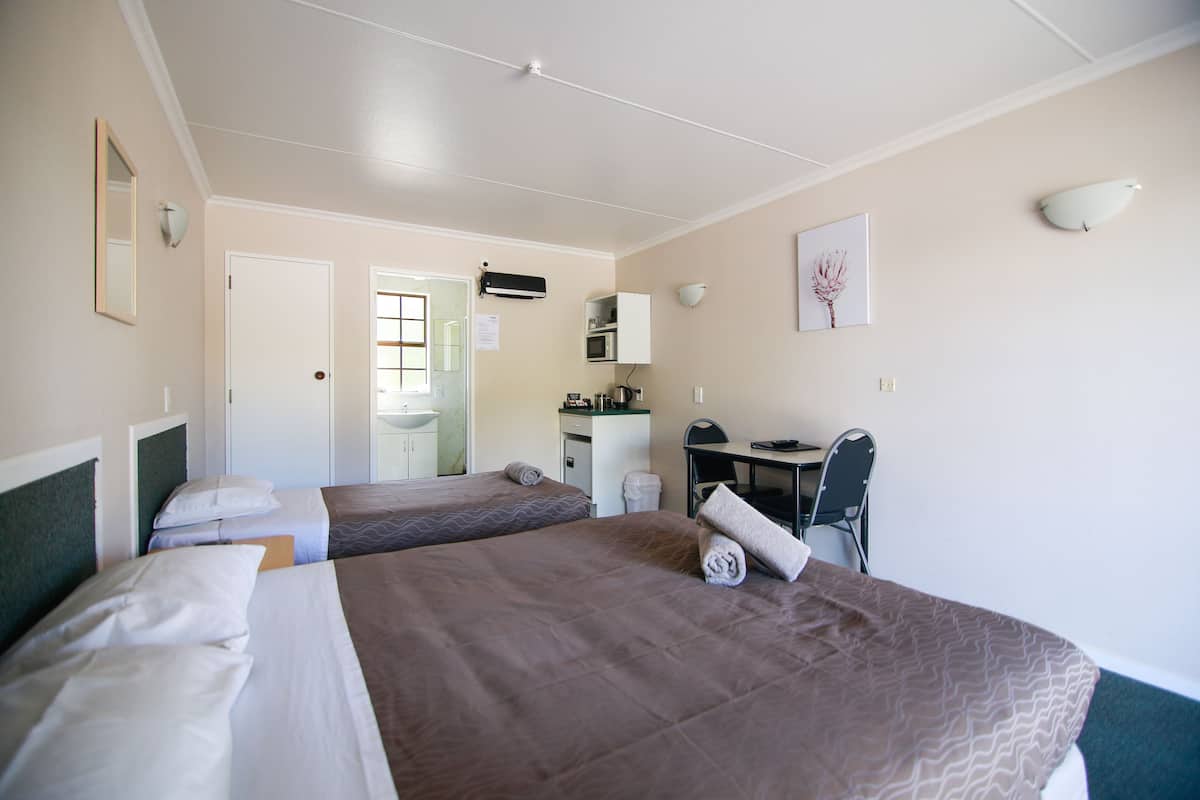 A hotel room with two beds, a desk, a chair, a sink, and a mirror.