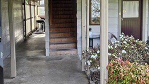Un escalier en bois menant à une porte, une petite table avec un pot de fleurs et un jardin planté de fleurs.