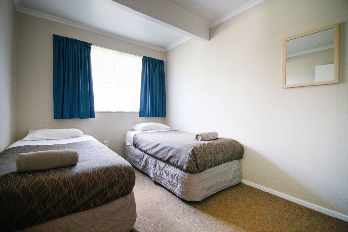 A hotel room with two single beds, a large window with curtains, a mirror, and a carpeted floor.