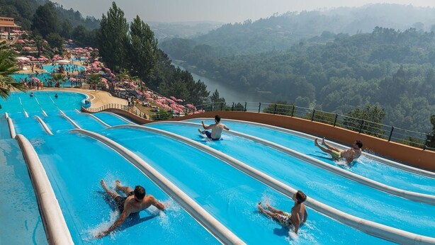 Een waterpark met verschillende glijbanen en een mooi uitzicht op een meer en bos.