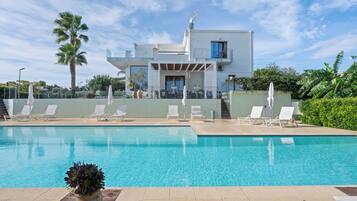 Un edificio moderno con piscina y sillones de descanso.