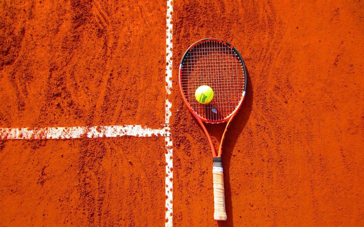 A tennis racket and ball on a clay court.