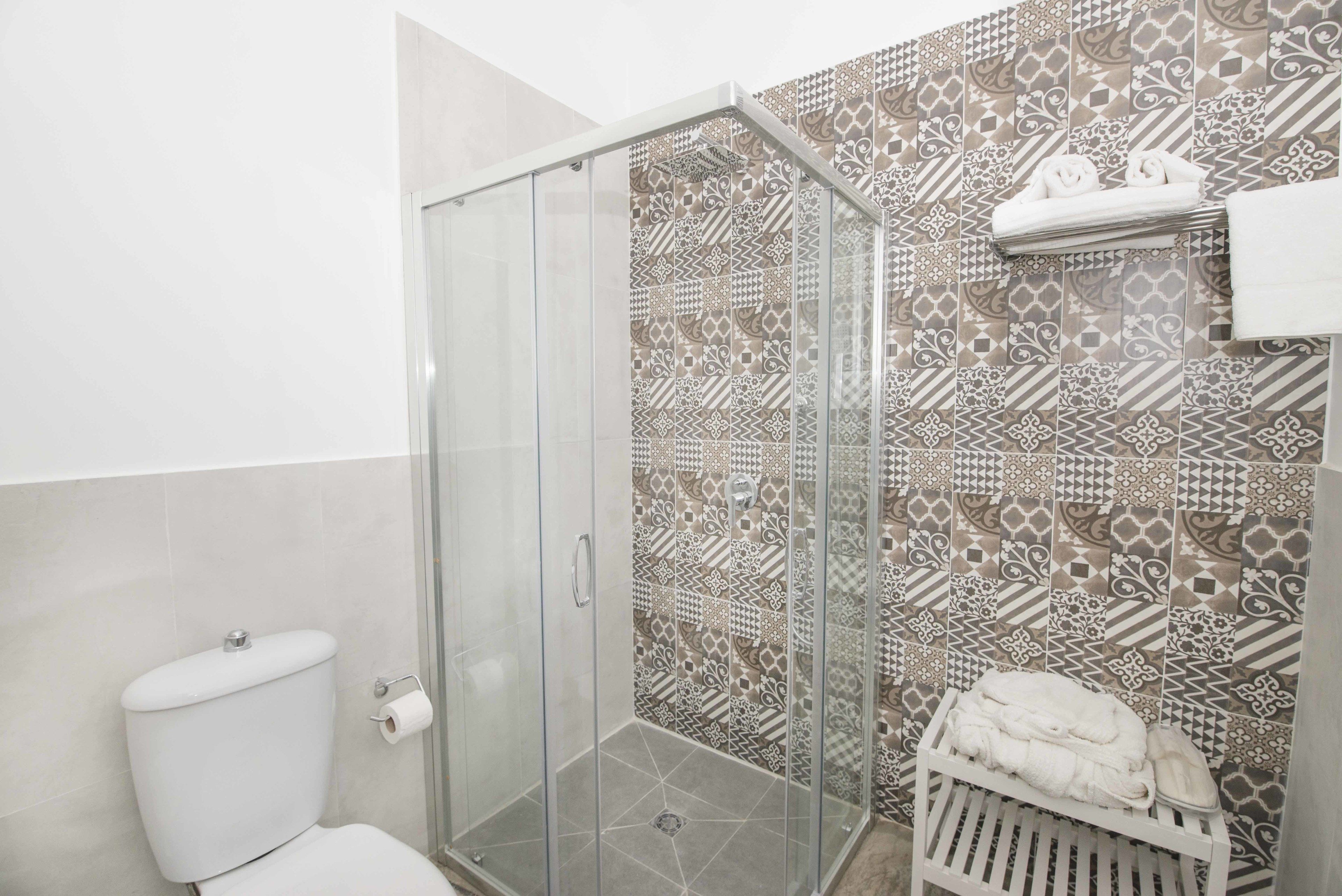 A bathroom with a glass shower enclosure, patterned tiles, a toilet, and a towel rack with towels.