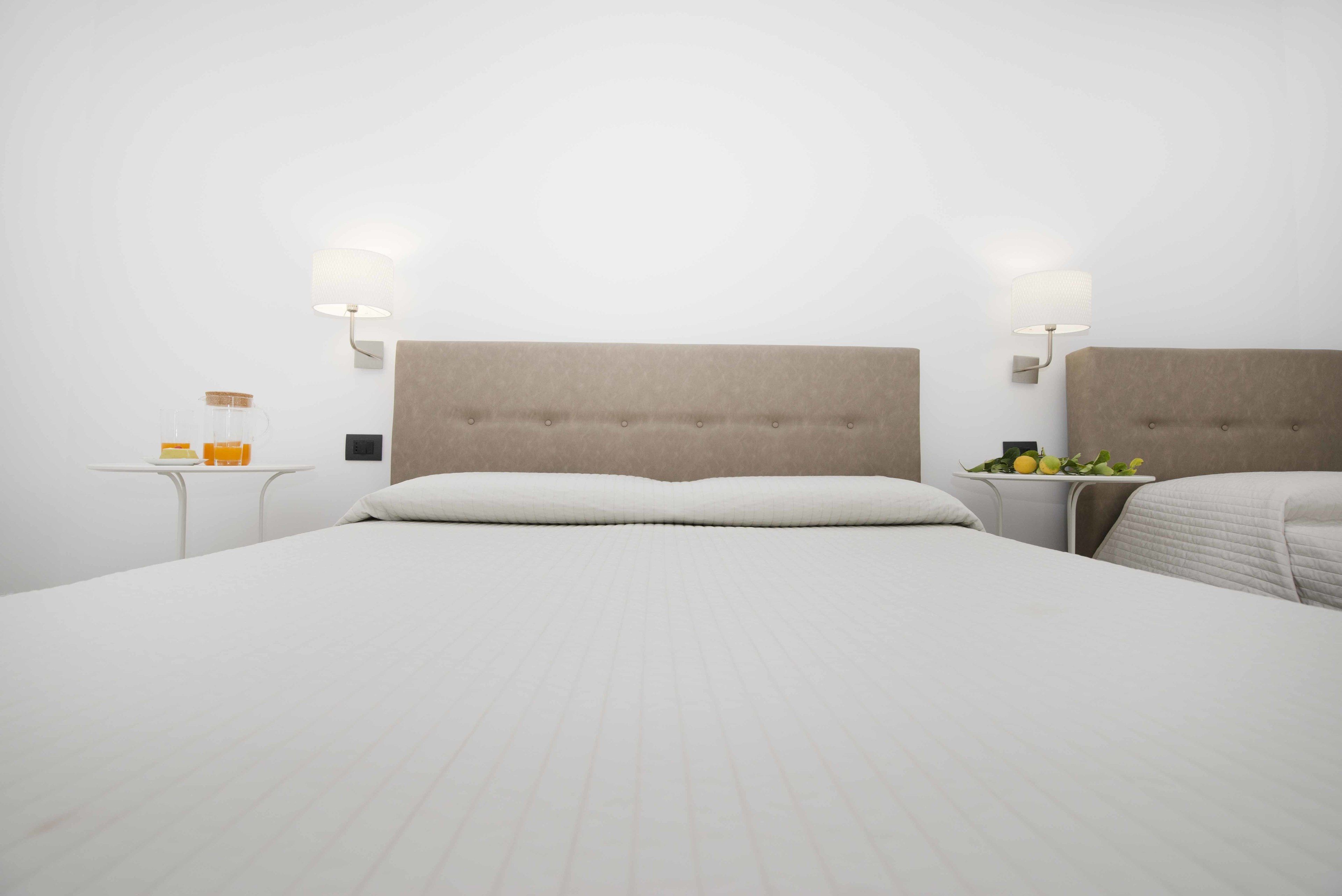 A hotel room with a large bed, two bedside tables, and wall-mounted lamps.
