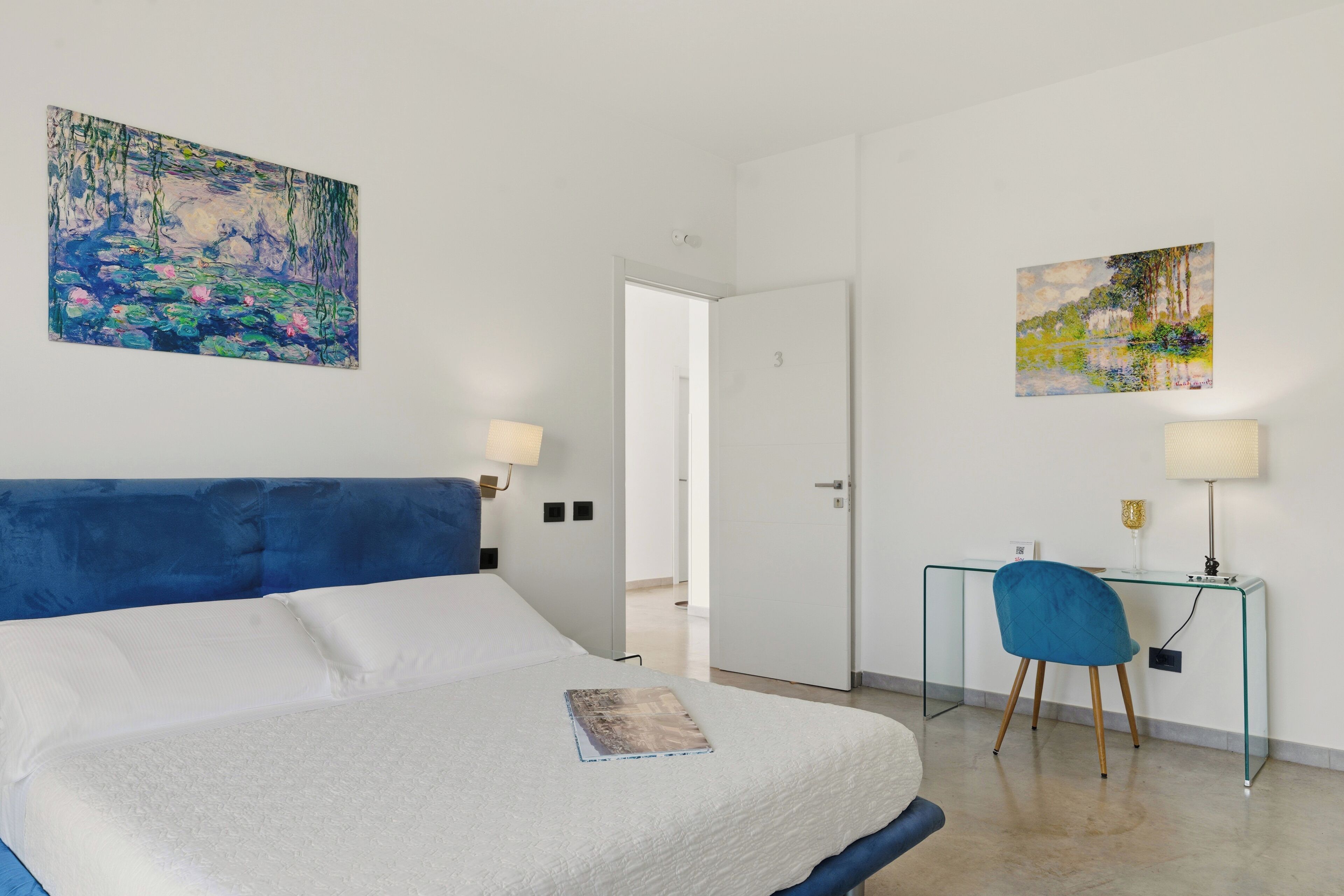 Camera d'albergo con un letto, una scrivania, due lampade e due quadri alle pareti.