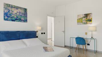 Camera d'albergo con un letto, una scrivania, due lampade e due quadri alle pareti.