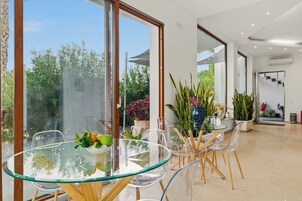 Un comedor moderno con una mesa de vidrio y sillas, rodeado de ventanas amplias y plantas de interior.