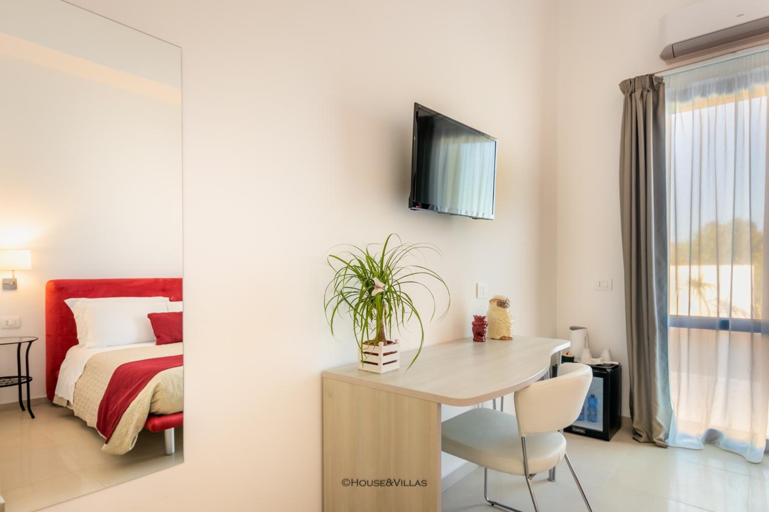 A modern hotel room with a bed, a desk, a chair, a TV, and a window with curtains.