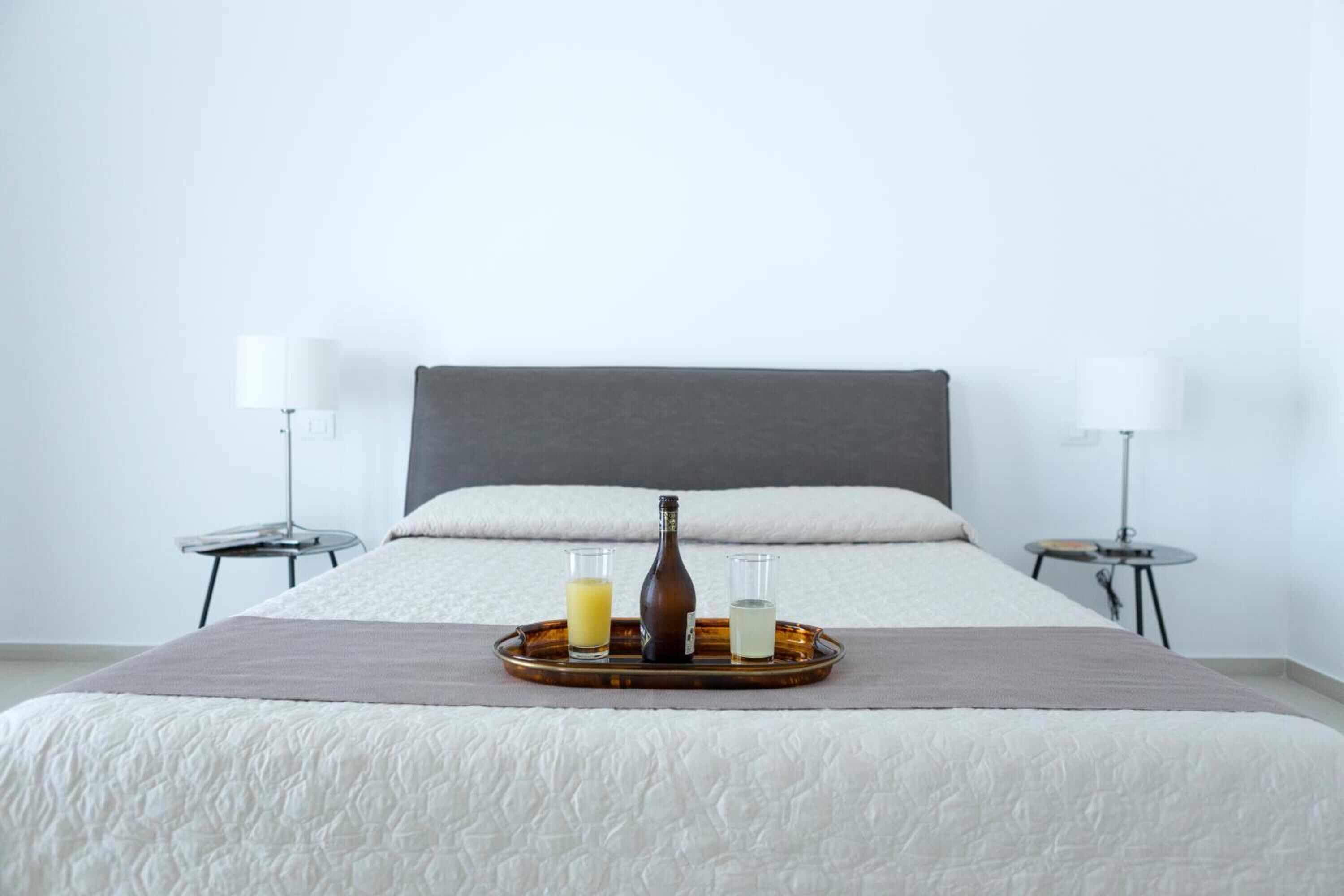 Un lit bien fait, avec un plateau de boissons et une bouteille, deux lampes de chevet et un mur sobre.