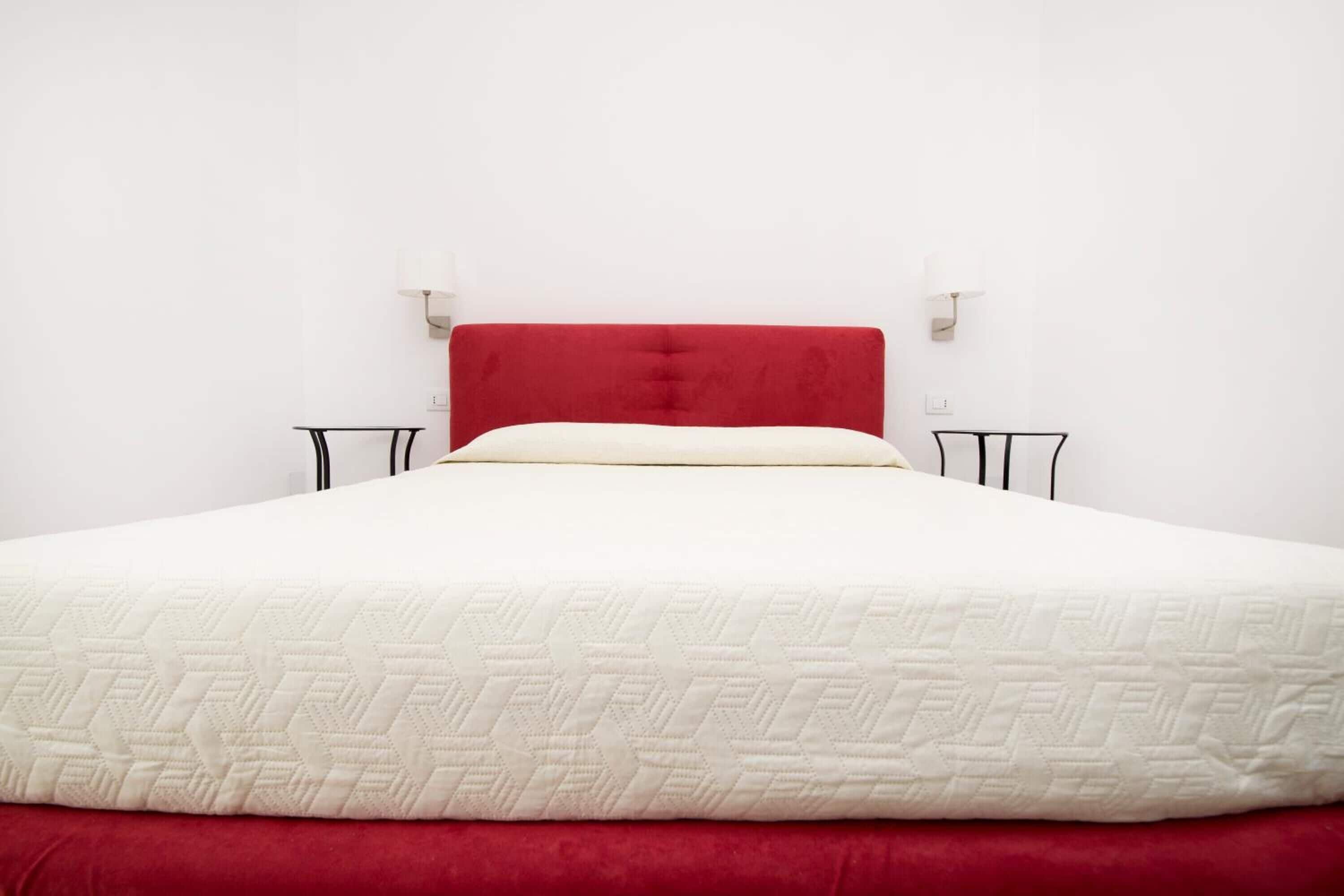 A bed with a red headboard, white bedding, and two bedside tables with black frames.