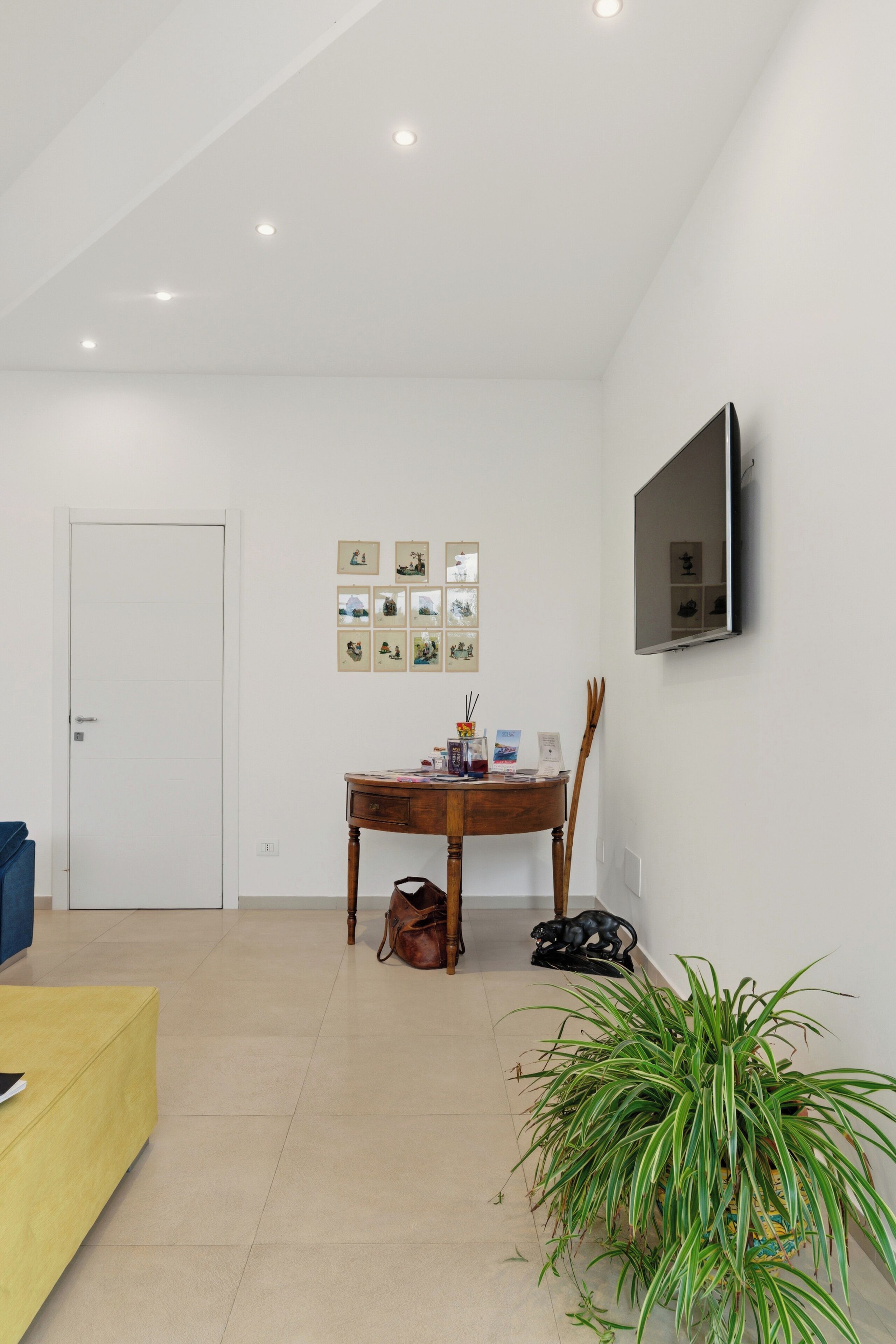 A modern living room with a dining table, a TV mounted on the wall, and a potted plant.