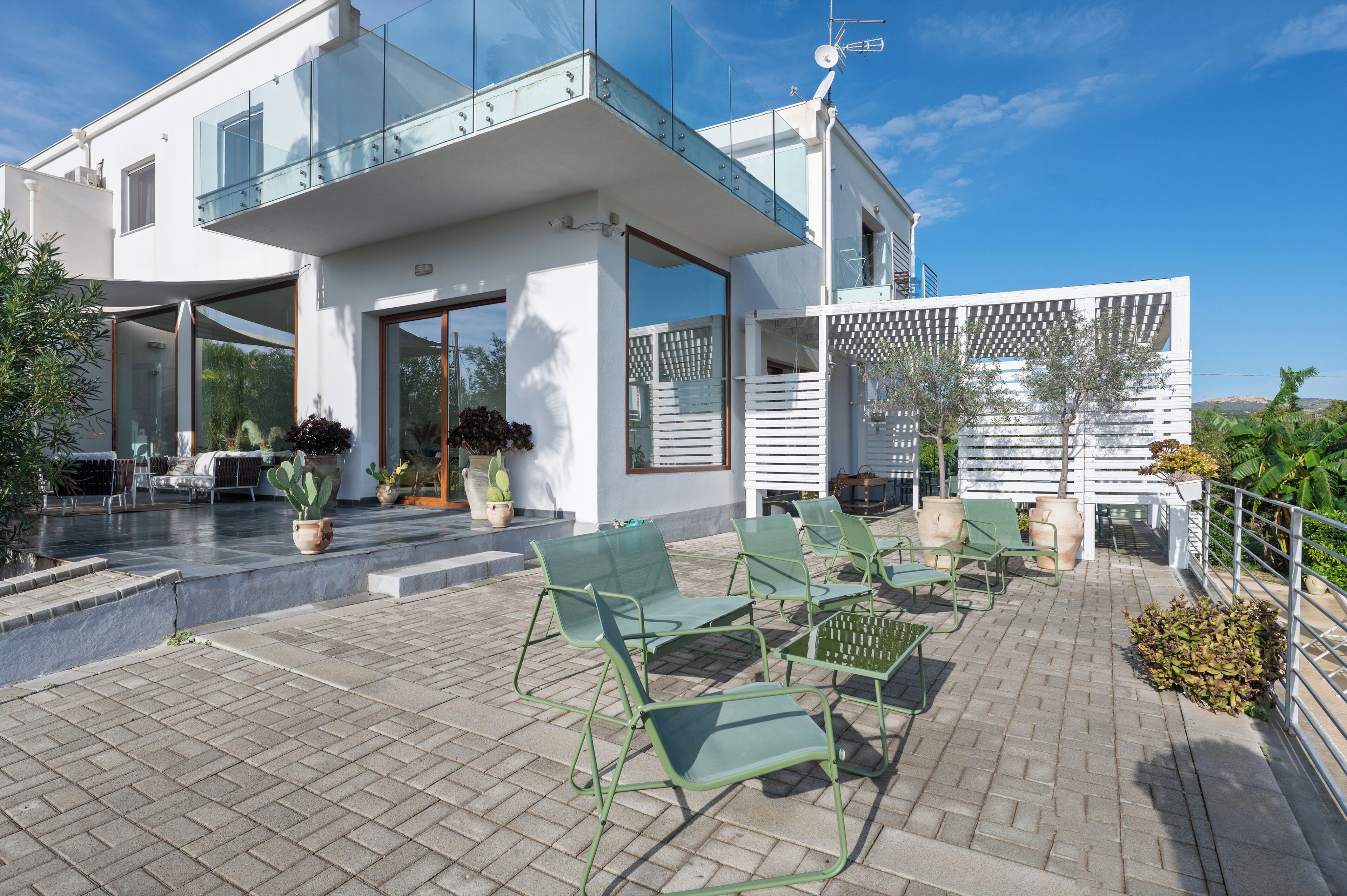 A modern house with a patio area featuring green chairs and potted plants.