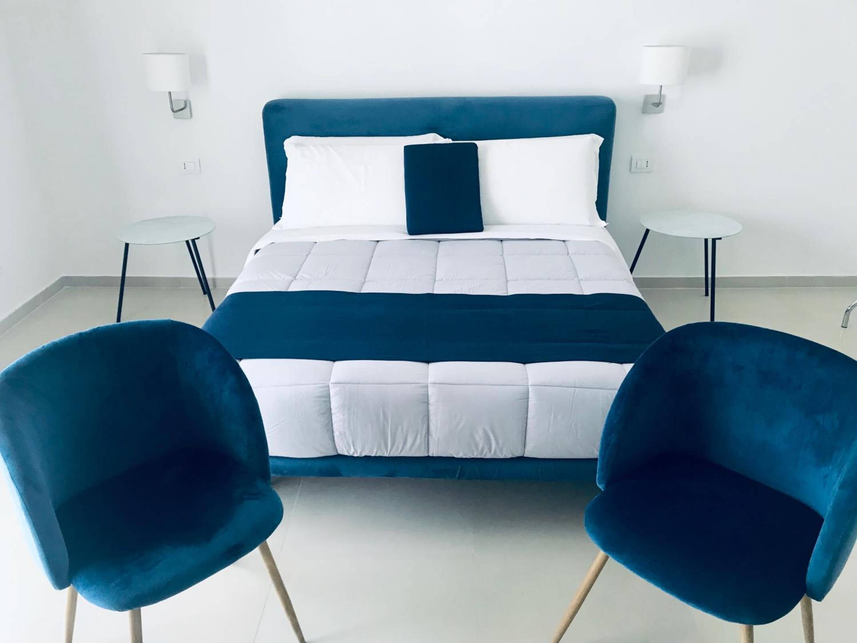 A modern bedroom with a large bed, two blue chairs, and bedside tables.