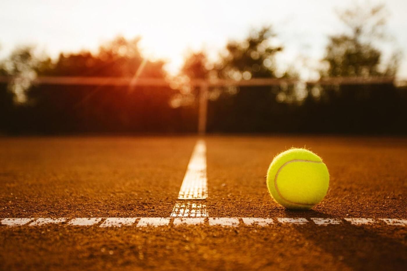 A tennis ball on a court with a net in the background.