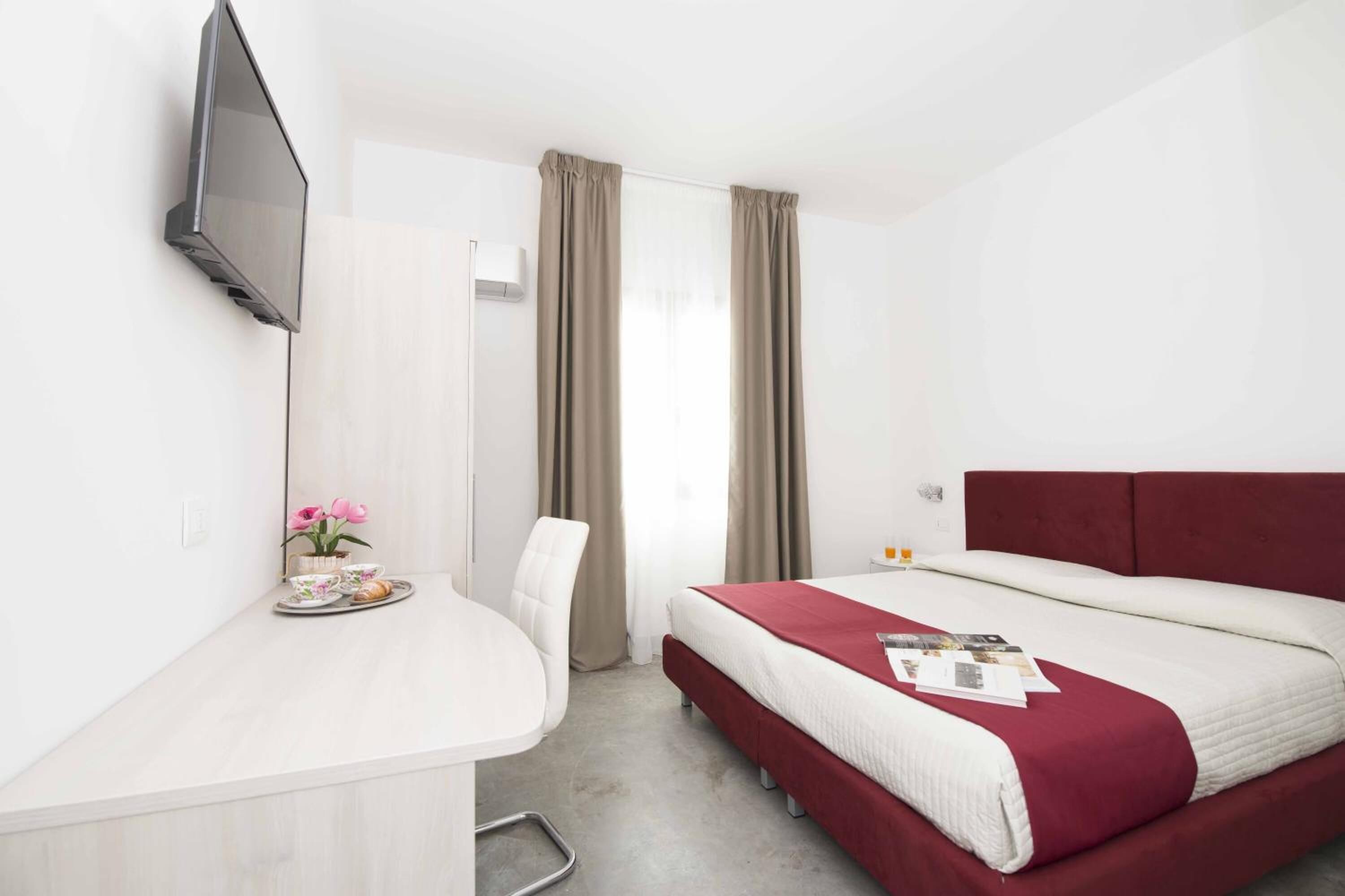 Ein Hotelzimmer mit Bett, Schreibtisch, Fernseher und einem Fenster mit Vorhängen.