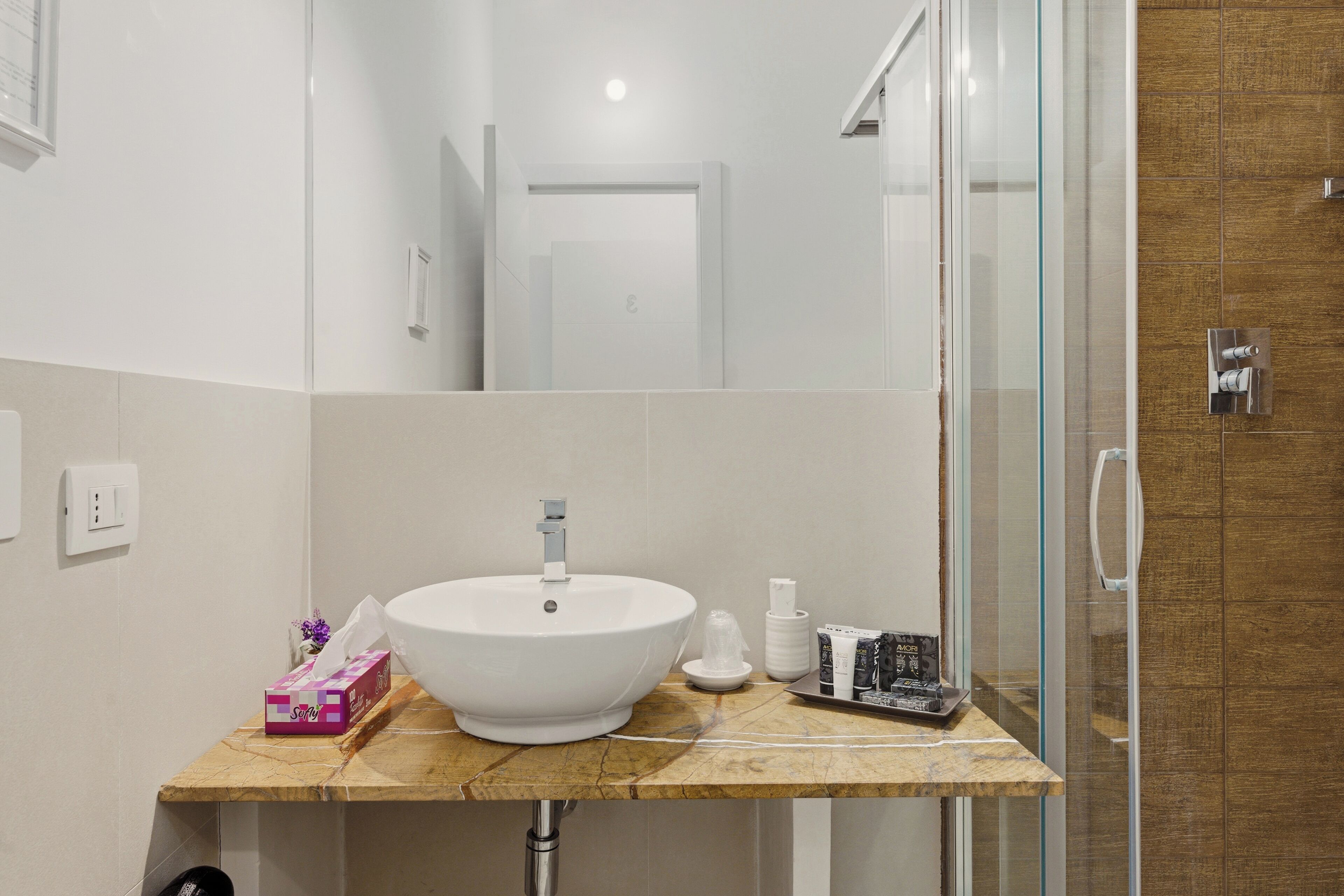 Un bagno con un lavandino bianco, uno spazio doccia in vetro e un piano di lavoro in marmo.