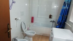 Une salle de bain comprenant des toilettes, un bidet, une baignoire et un lavabo blanc.