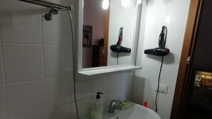Une salle de bain avec un lavabo blanc, un miroir et un sèche-cheveux fixé au mur.