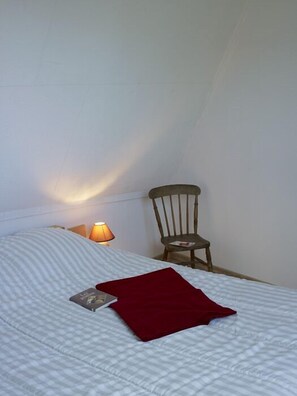 A bedroom with a bed, a wooden chair, and a nightstand with a lamp. - Beautiful Breton farmhouse, Pink Granite Coast, sleeps 8, near beaches (Trébeurden)