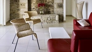Un salon avec une cheminée en pierre, des fauteuils en osier, un canapé rouge et une table basse blanche.