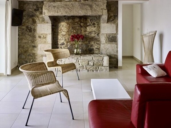 Una sala de estar con chimenea de piedra, sillones de mimbre, un sofá rojo y una mesa de centro blanca.