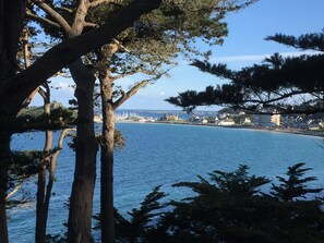 A coastal view with trees framing the scene, a body of water, and buildings in the distance. - Beautiful Breton farmhouse, Pink Granite Coast, sleeps 8, near beaches (Trébeurden)