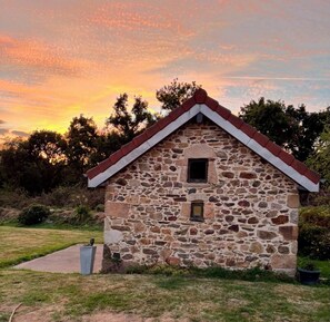 Un bâtiment en pierre avec un toit rouge, une petite fenêtre et un jardinier en béton orné d’une sculpture.
