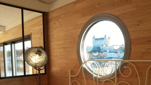 A room with wooden walls, a round window with a view of a castle, and a floor lamp.