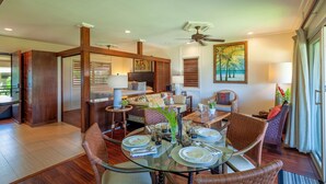 A dining area with a glass table set for four, surrounded by wicker chairs. There is a ceiling fan above and a painting of palm trees on the wall. - Steps from the sand, beach front and secludedon Kauai's north shore (Hanalei)