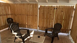 En terrasse med to Adirondack-stole og et lille bord, omkranset af et træhegn.