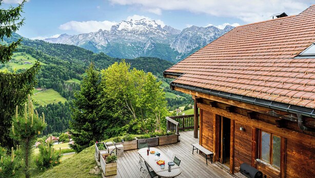 A wooden cabin with a deck overlooking a mountainous landscape.