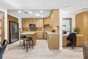 Une cuisine moderne avec des meubles en bois, des appareils en acier inoxydable, un îlot central doté de tabourets et un four à micro-ondes encastré.