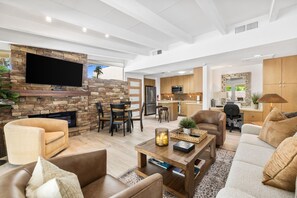 A modern living room with a stone fireplace, a flat-screen TV, comfortable seating, and a kitchen area in the background. - El Paseo, 'The Rodeo Drive of Beverly Hills' In Palm Desert. Free  Wi FI (Palm Desert)